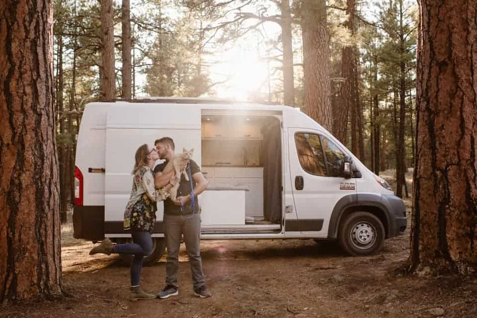 A portrait of a couple kissing holding a cat in front of a van.