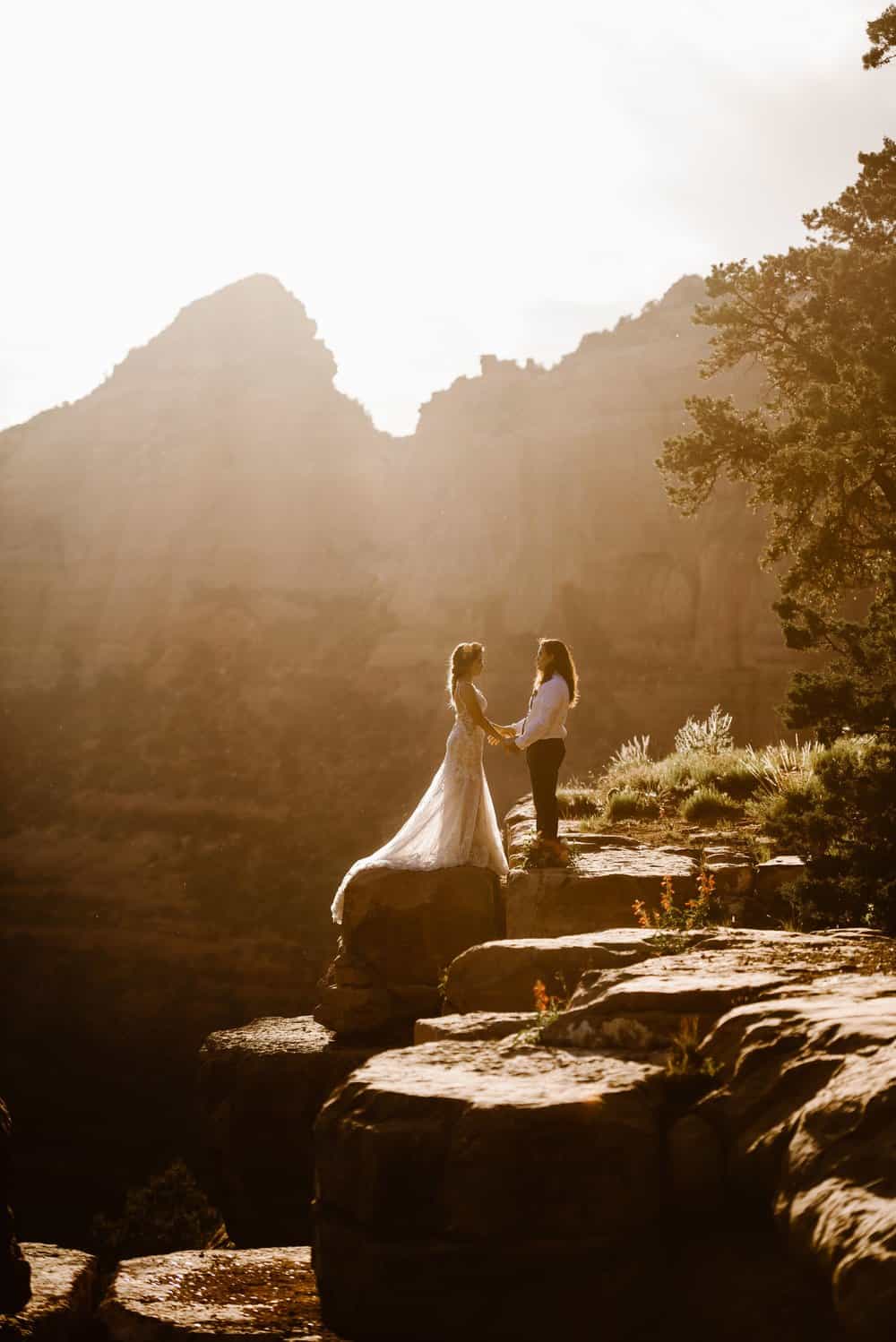 A bride hold hands and look at each other as the sun sets behind them.