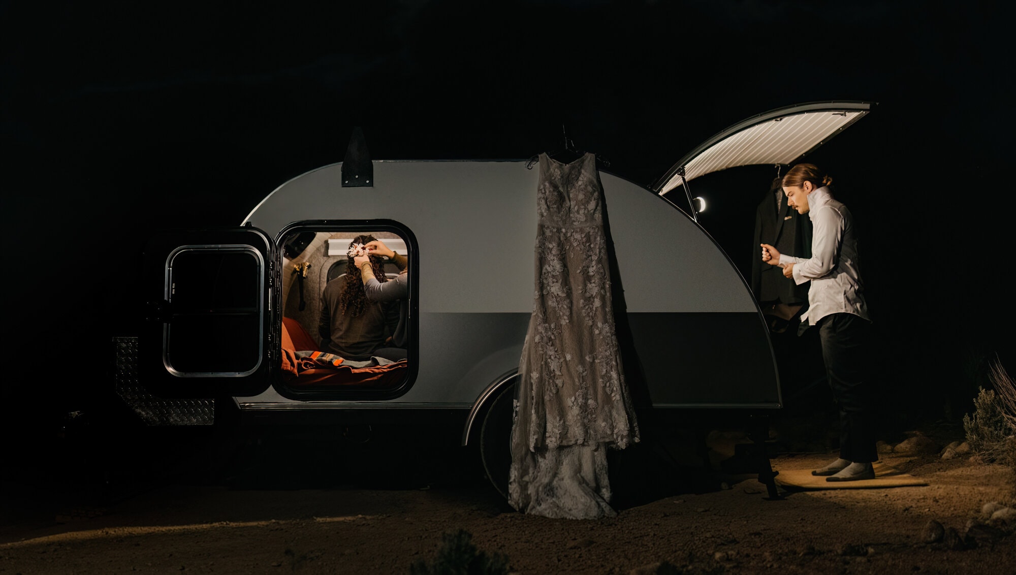 A bride and groom get ready outside of their trailer at camp.