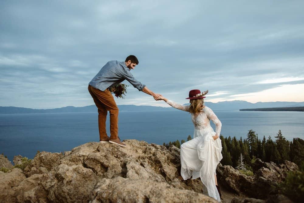 A groom assists his bride in getting up the rocks in her wedding dress.