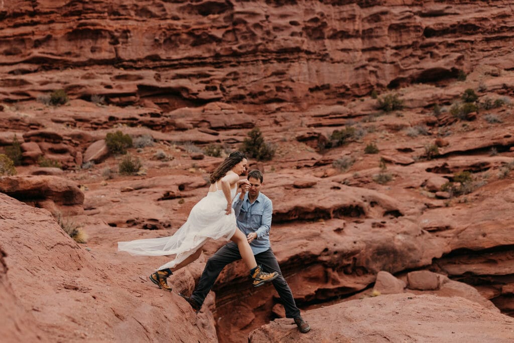 The couple jumps together across the rocks.