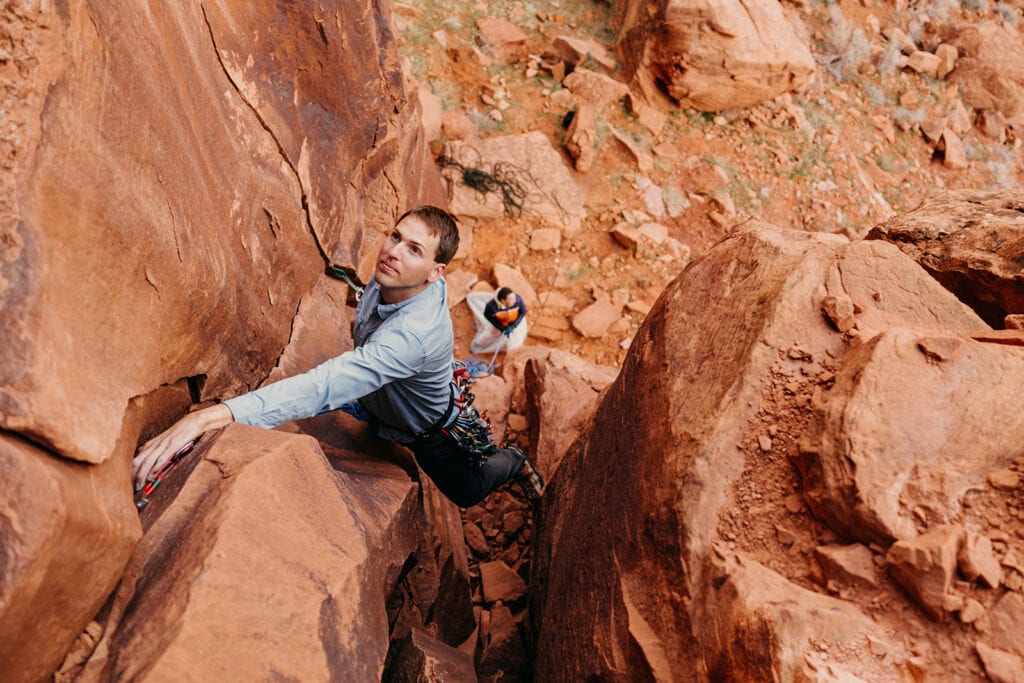 The groom has his hand in a crack as he looks up at the rest of the route.