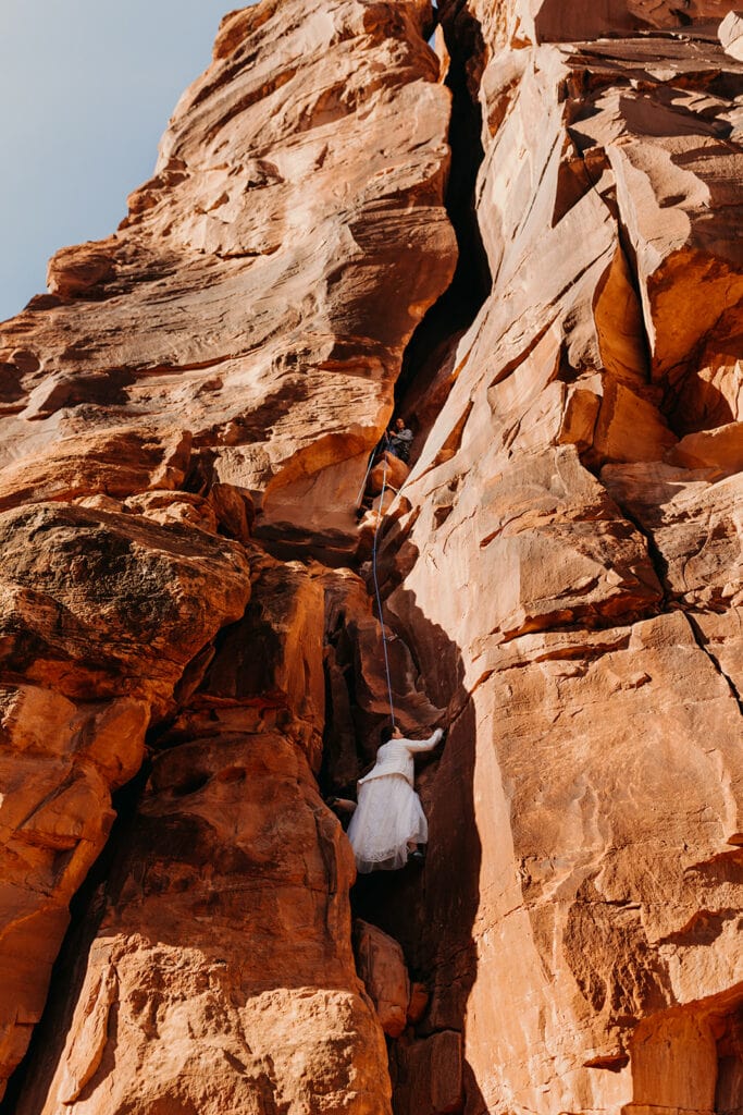 The bride climbs her way up the route towards the groom who is belaying her in the crack.