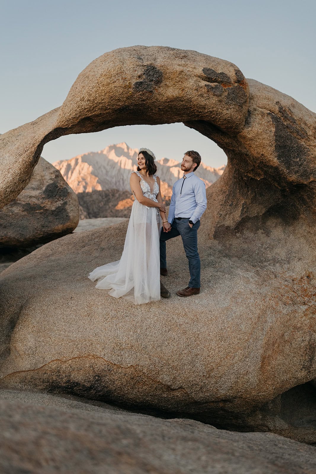 A couple watches sunrise while standing in a Mobius Arch.