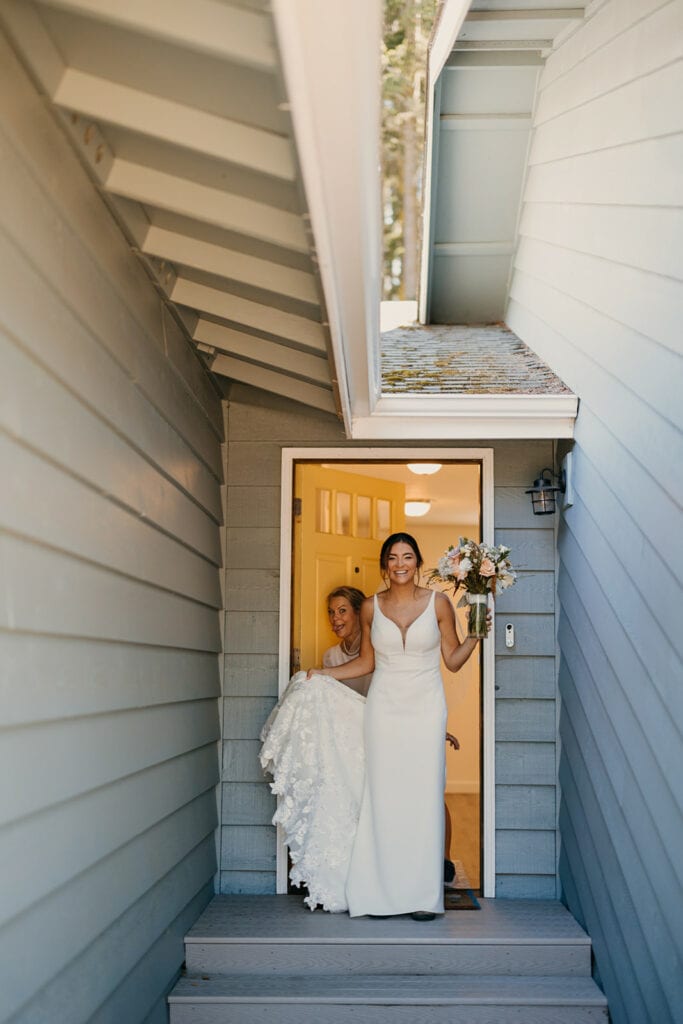 The bride leaves the house as her mom smiles behind her.