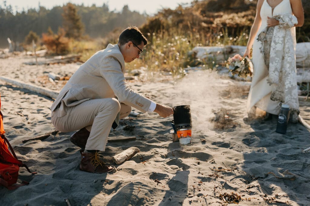 The groom prepares coffee on the beach at sunrise.