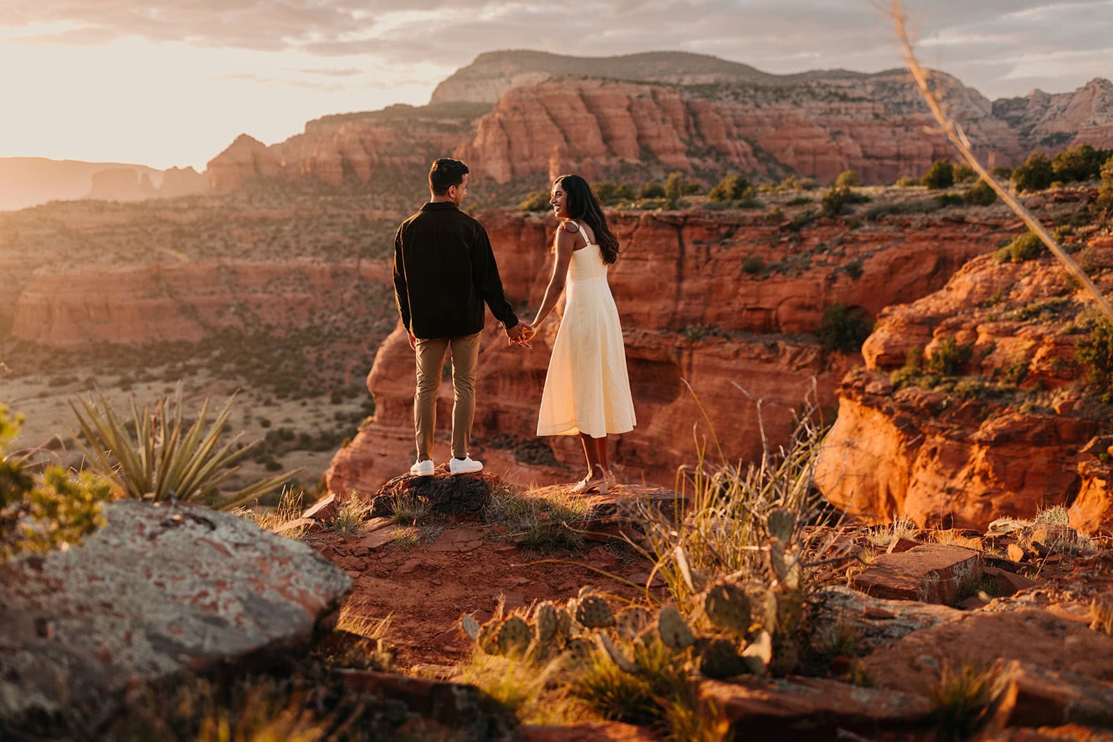 A newly engaged woman smiles at her partner as they watch sunset in the desert together.