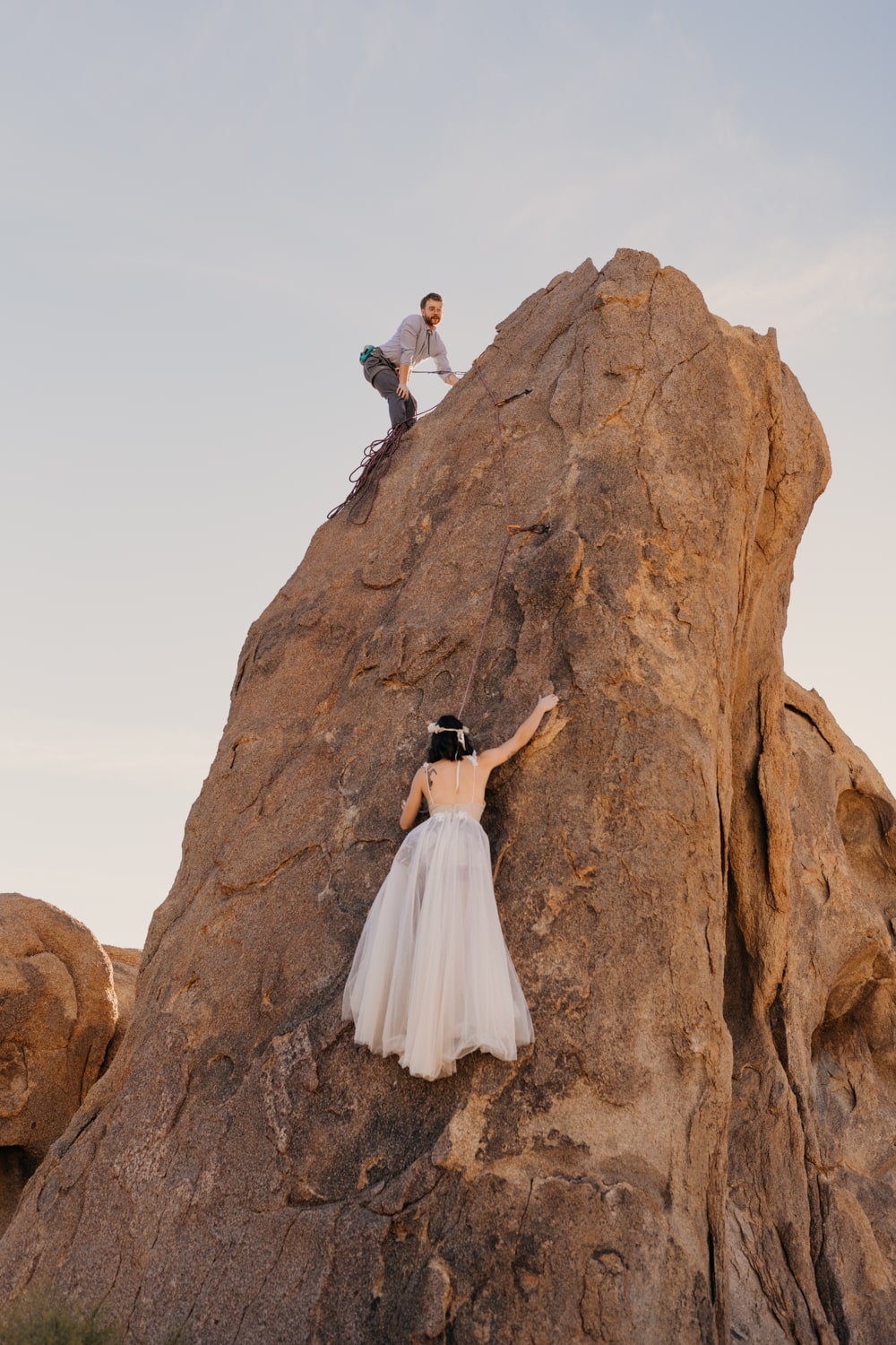 A bride climbs up a rock in her wedding dress.