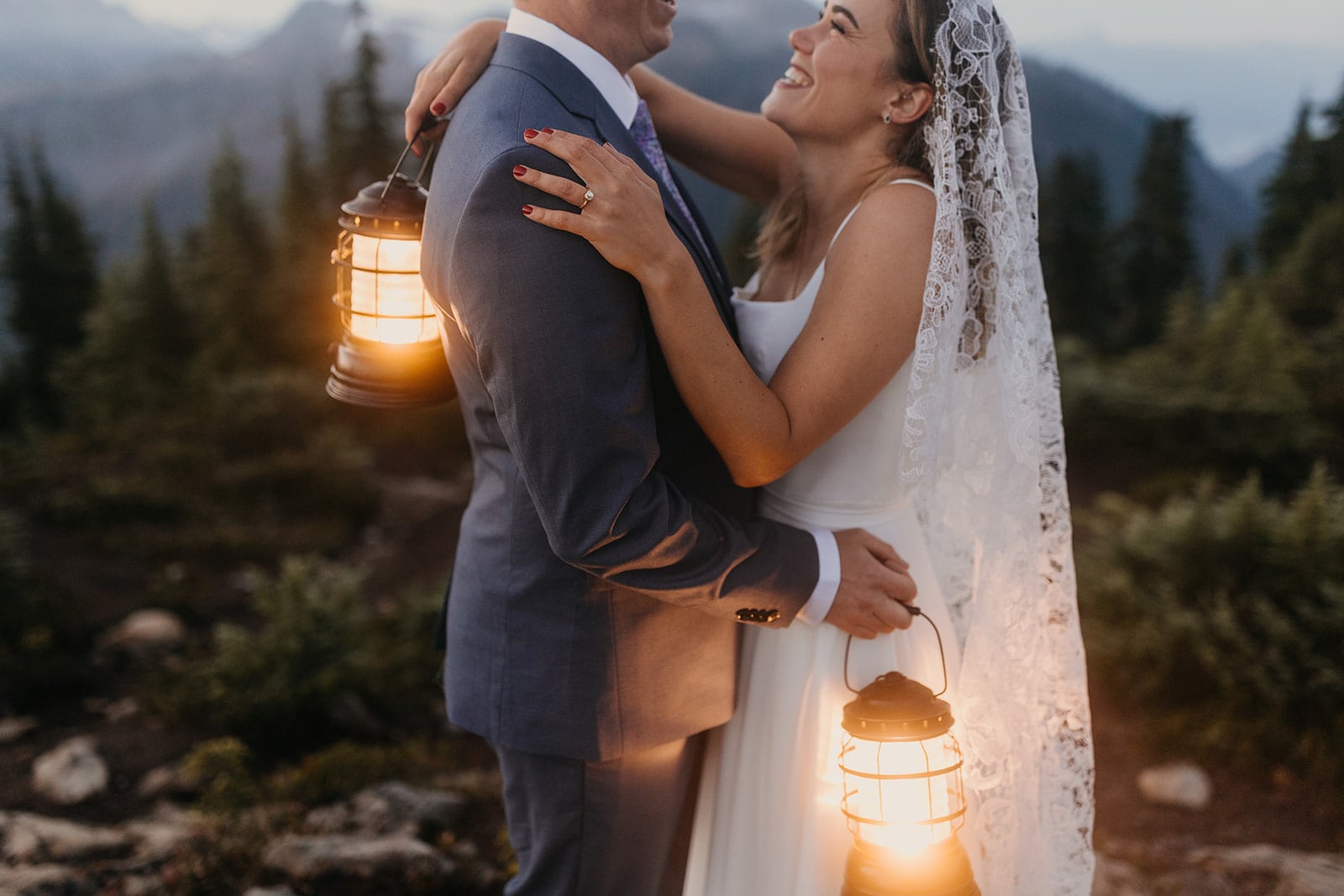 The bride smiles at the groom while they hold lanterns in the early am.