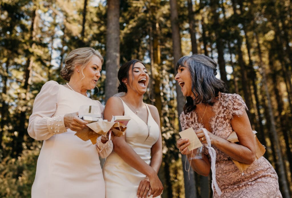 The bride gives her mom and the grooms mom a gift as they share a laugh together.