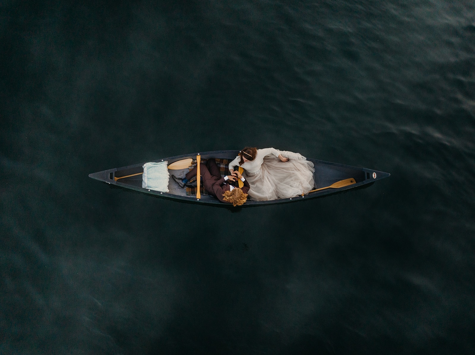 A couple sit together in a canoe on a lake on their wedding day.