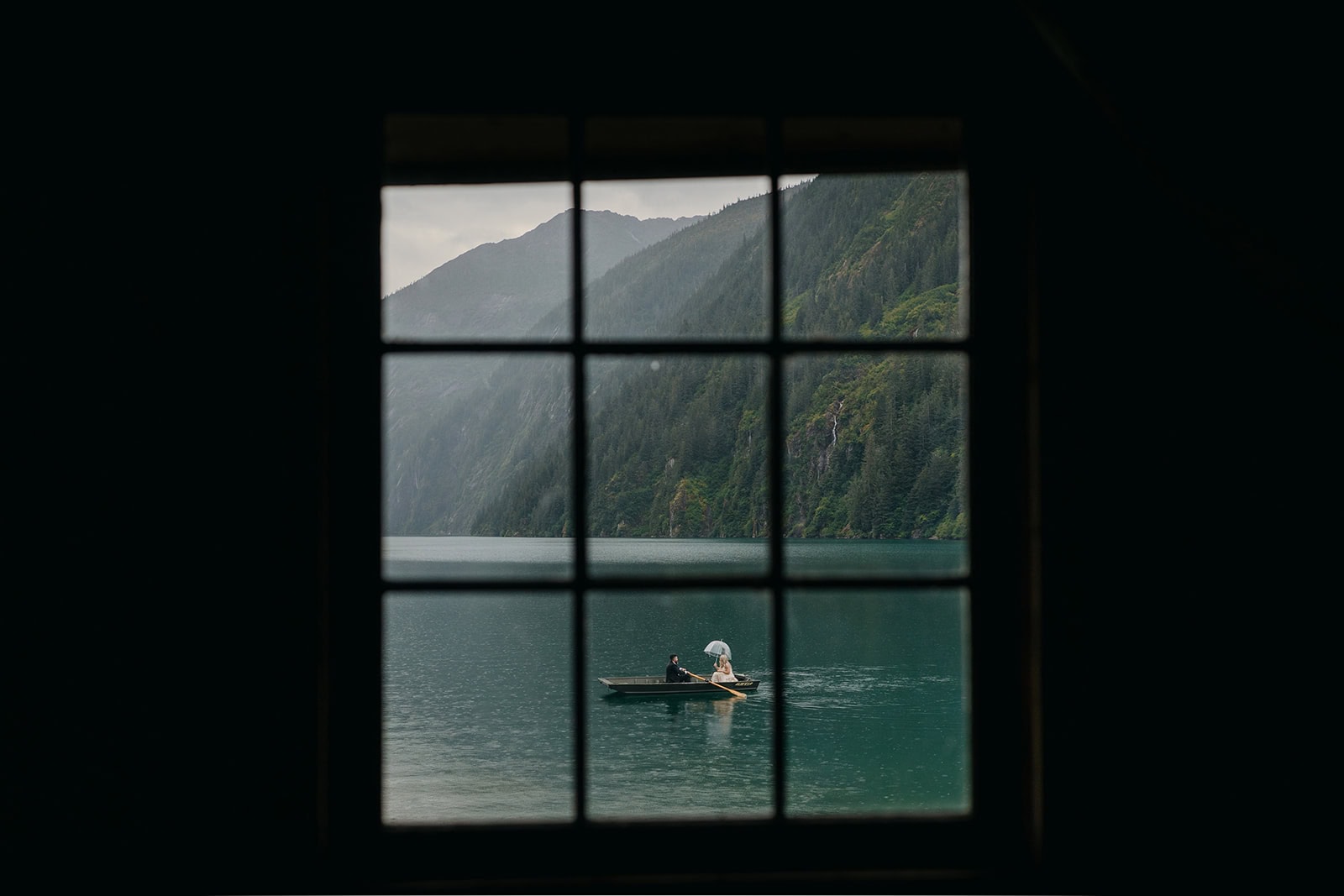 A couple paddles in the sound off of the coast of Juneau as the photographer takes a photo through the cabin's windows.