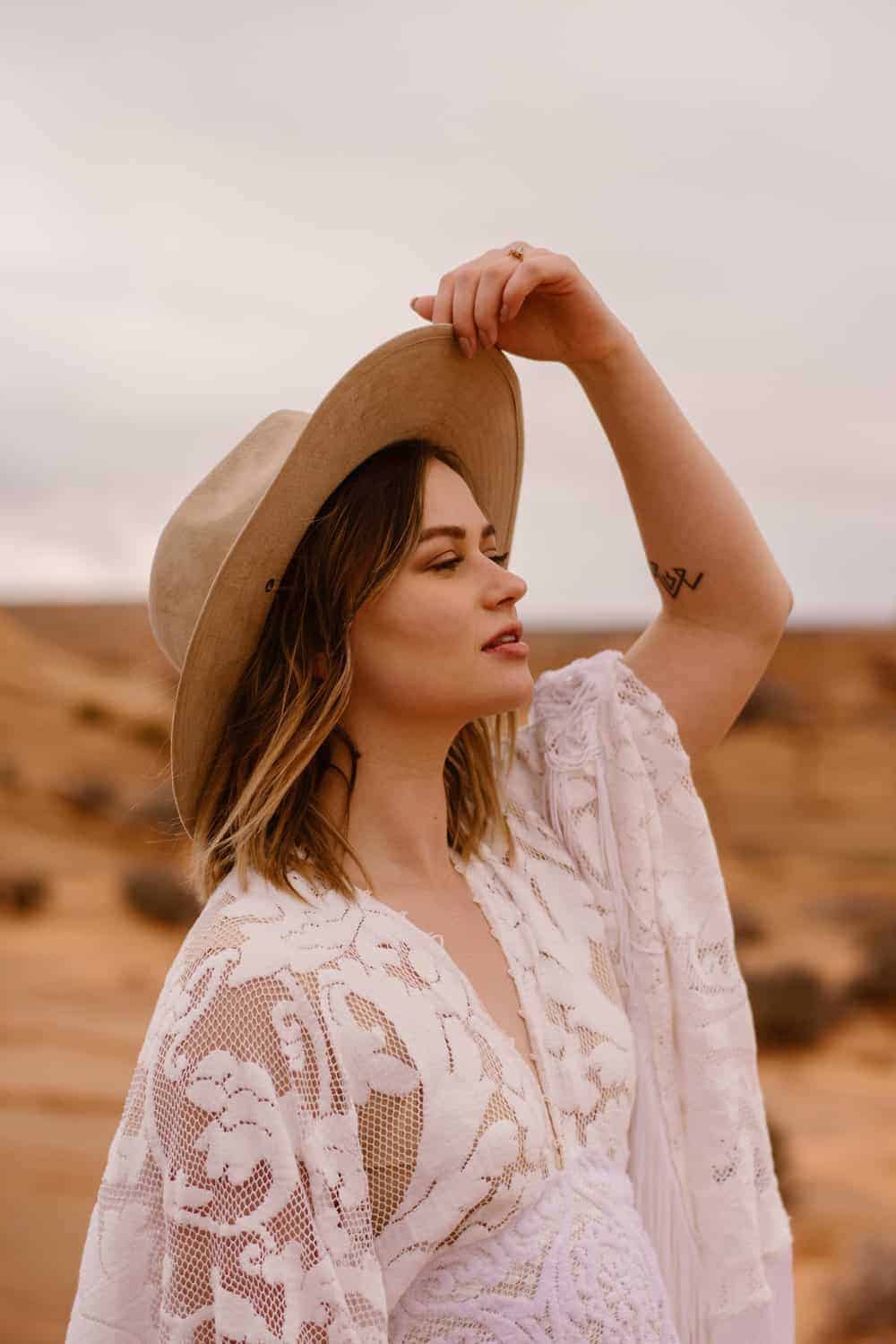 A bride holds her hat as she looks out towards the desert.