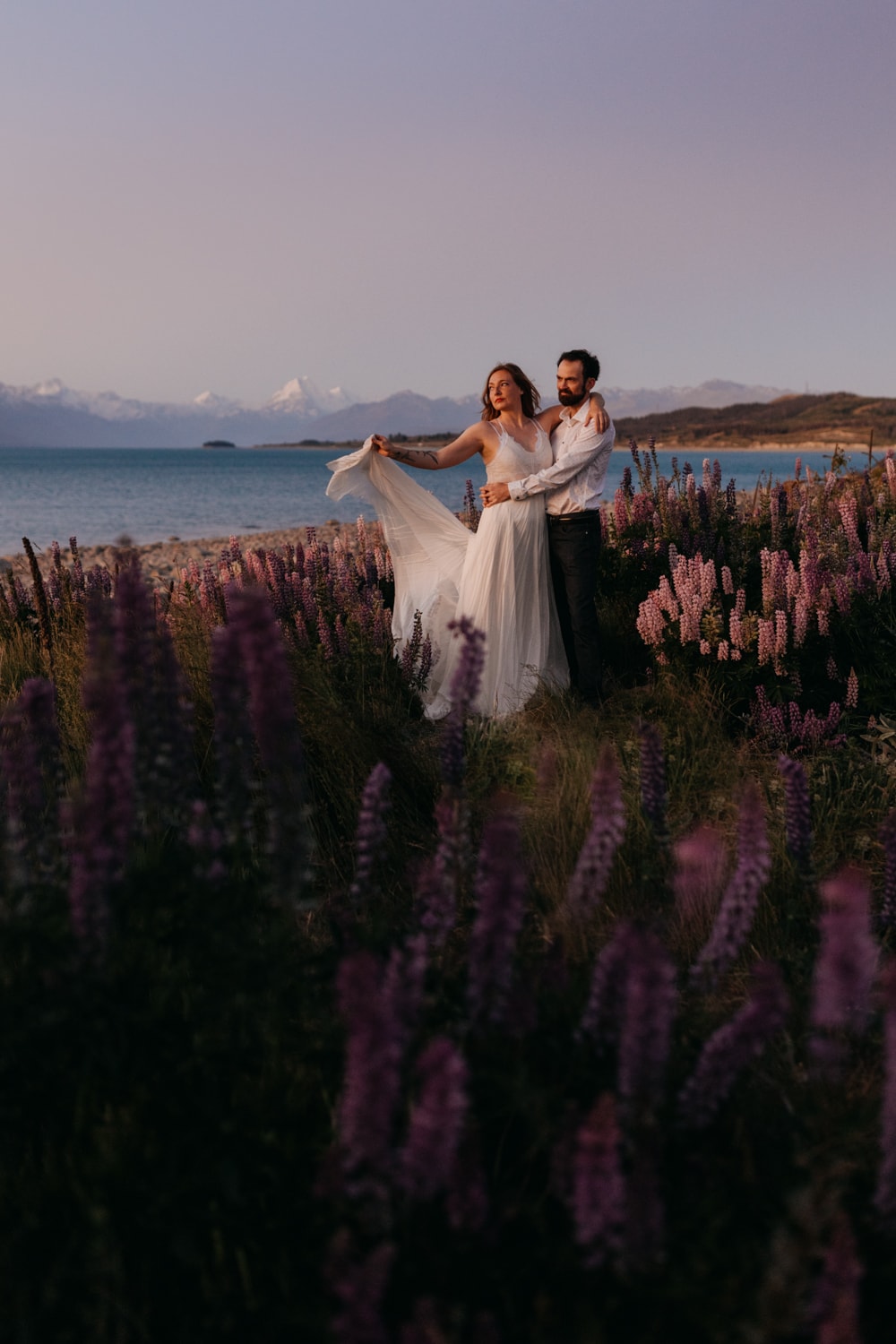 A couple watches sunset by the lake with Mt Cook in the background.