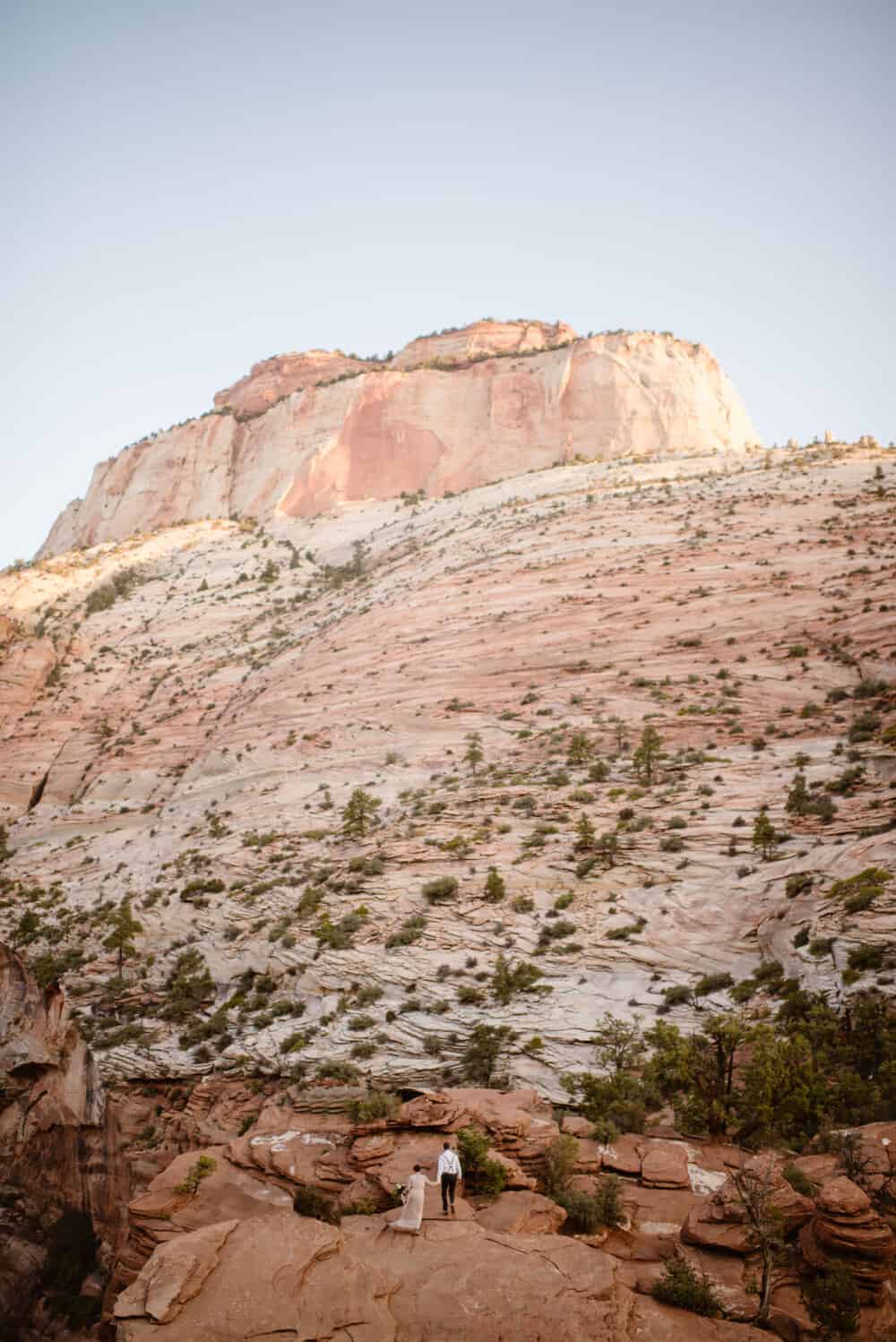 The bride and groom walk hand in hand while out at an overlook while within Zion National Park.