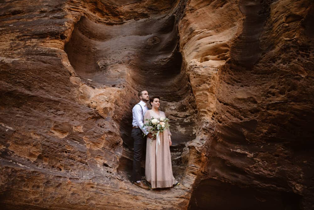 The bride and groom stand together in a moody slot canyon pocket within Zion National Park.
