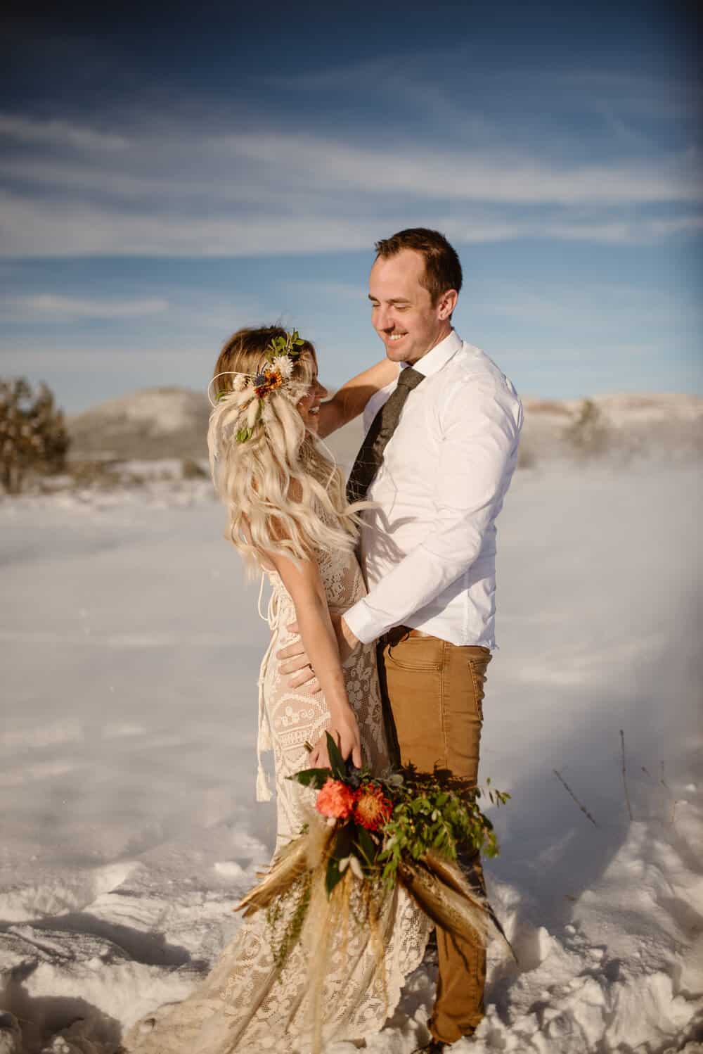 A groom smiles at his bride on a sunny day in the winter.