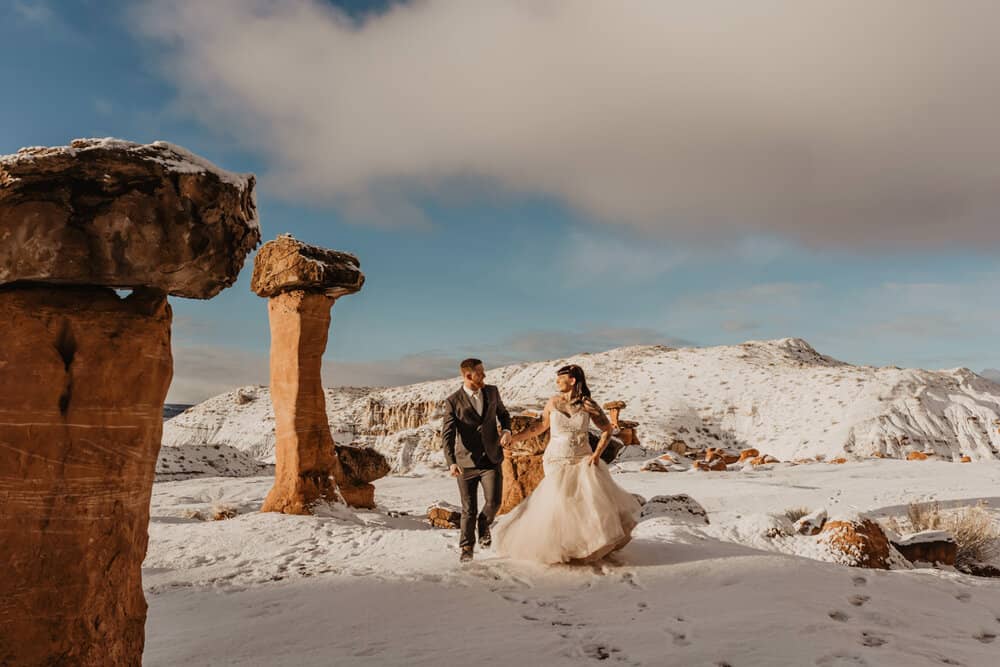 A couple walks through the snow together in the desert.