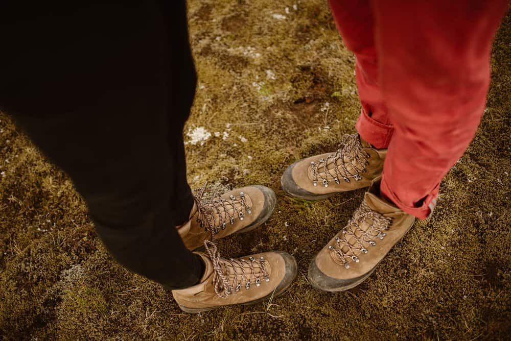 A couples pair of hiking boots on their feet as they stand on moss.