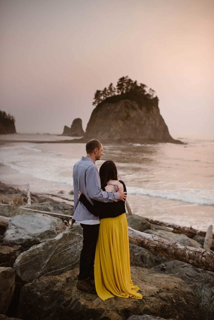 A couple stand together near sunset on the Olympic coast line looking out over the ocean.