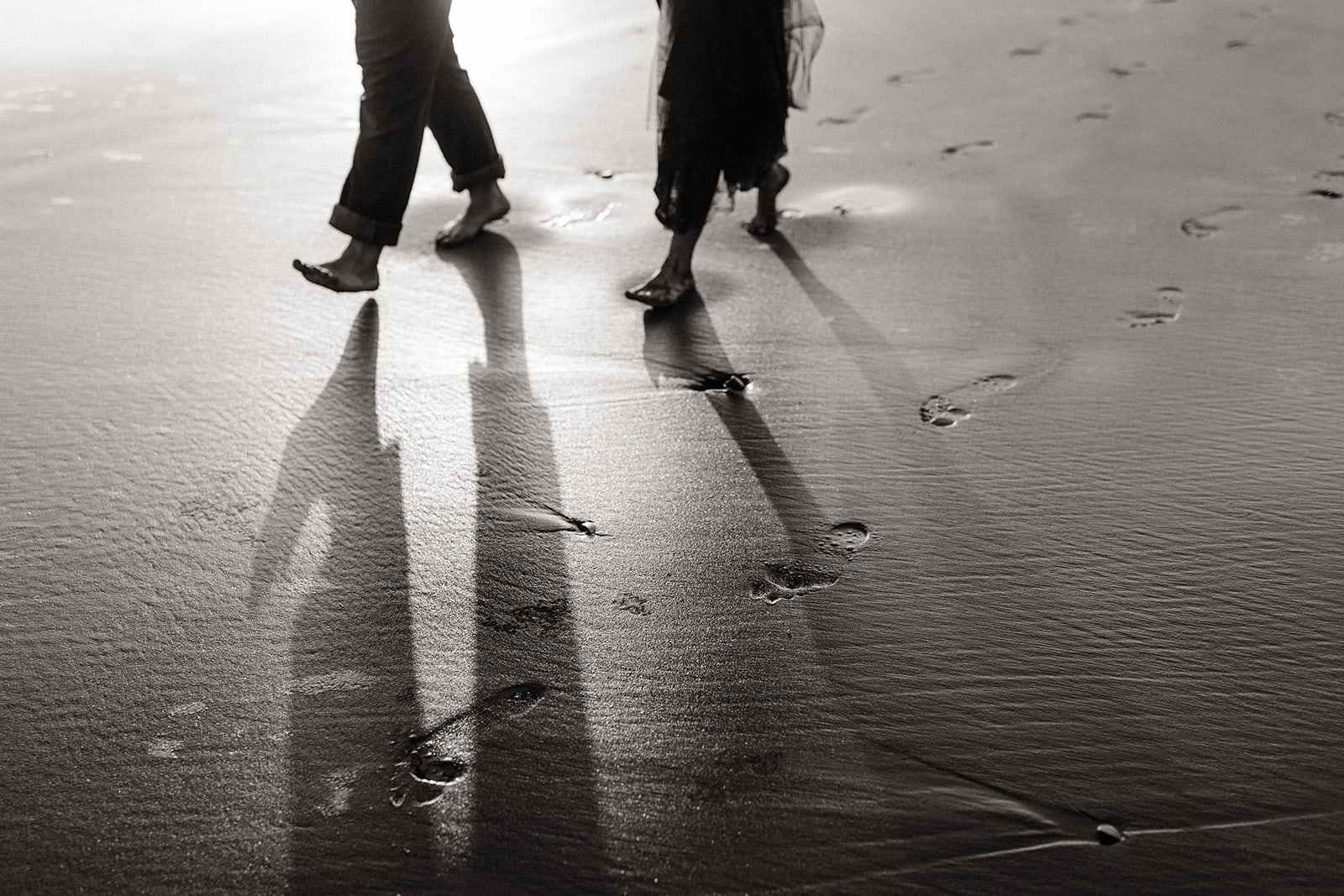 A couple makes foot prints together in the sand.
