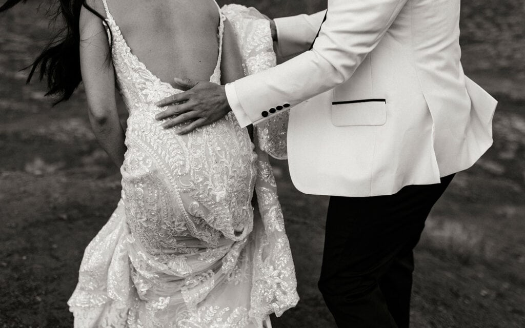The groom assists the bride as she hikes through the desert.
