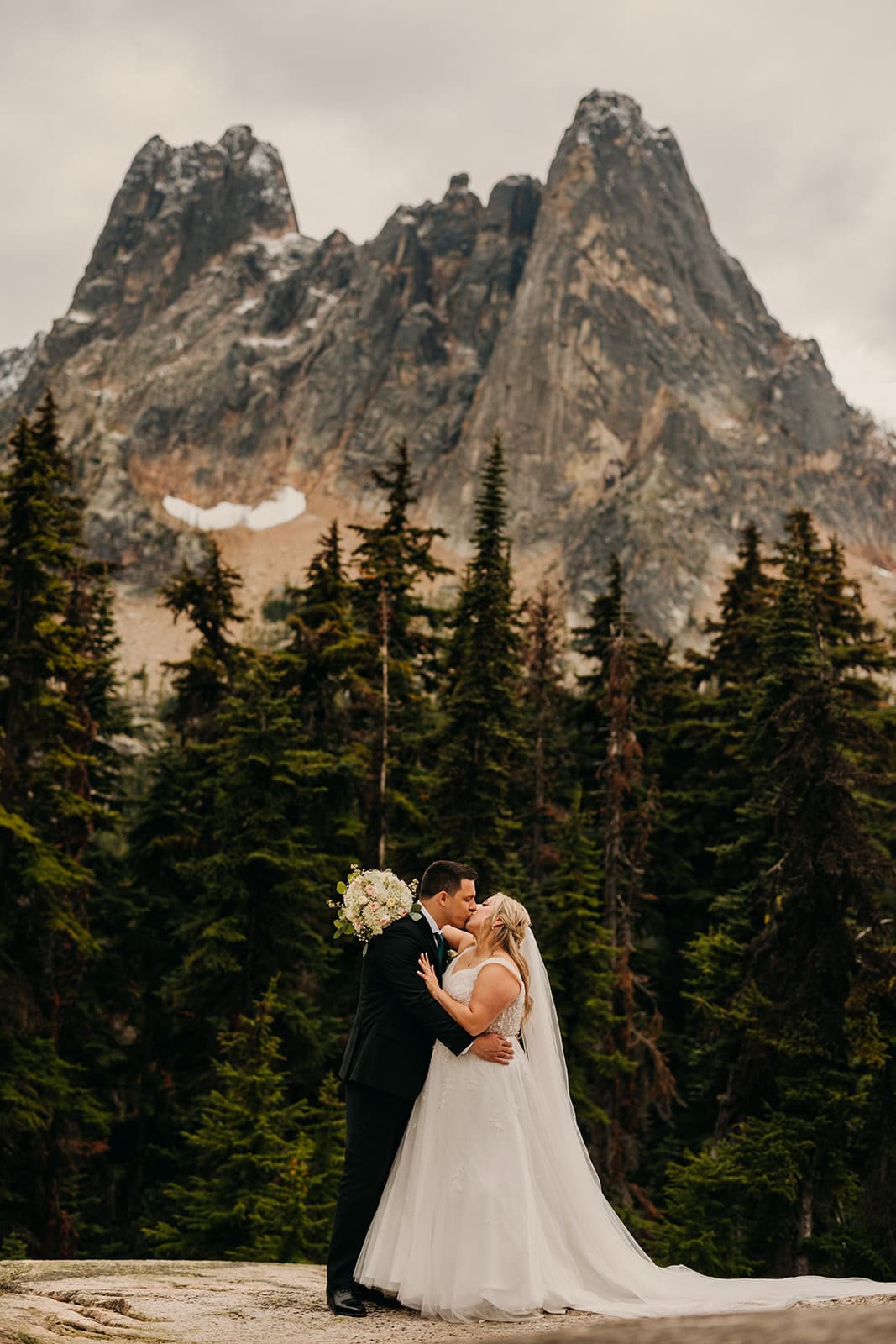 A couple shares a kiss standing in front of Liberty Bell mountain in the North Cascades.