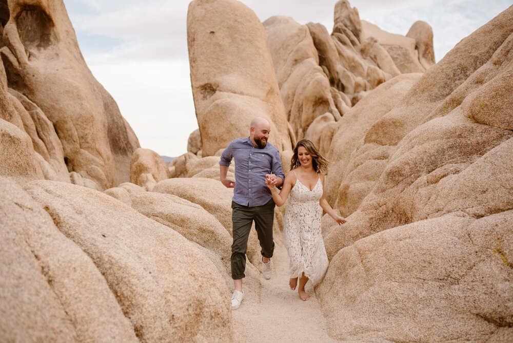 A couple runs through the rocks of Joshua Tree together smiling ear to ear.