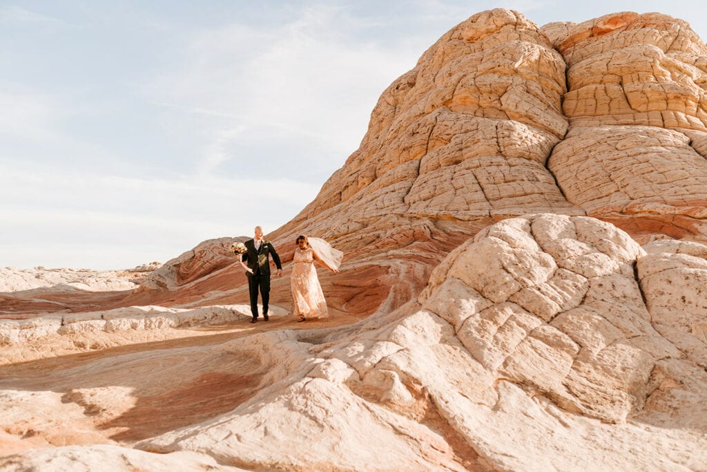 A bride and groom hold hands and walk on the white rock.