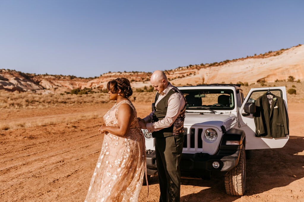A groom help zips a bride into her wedding dress.