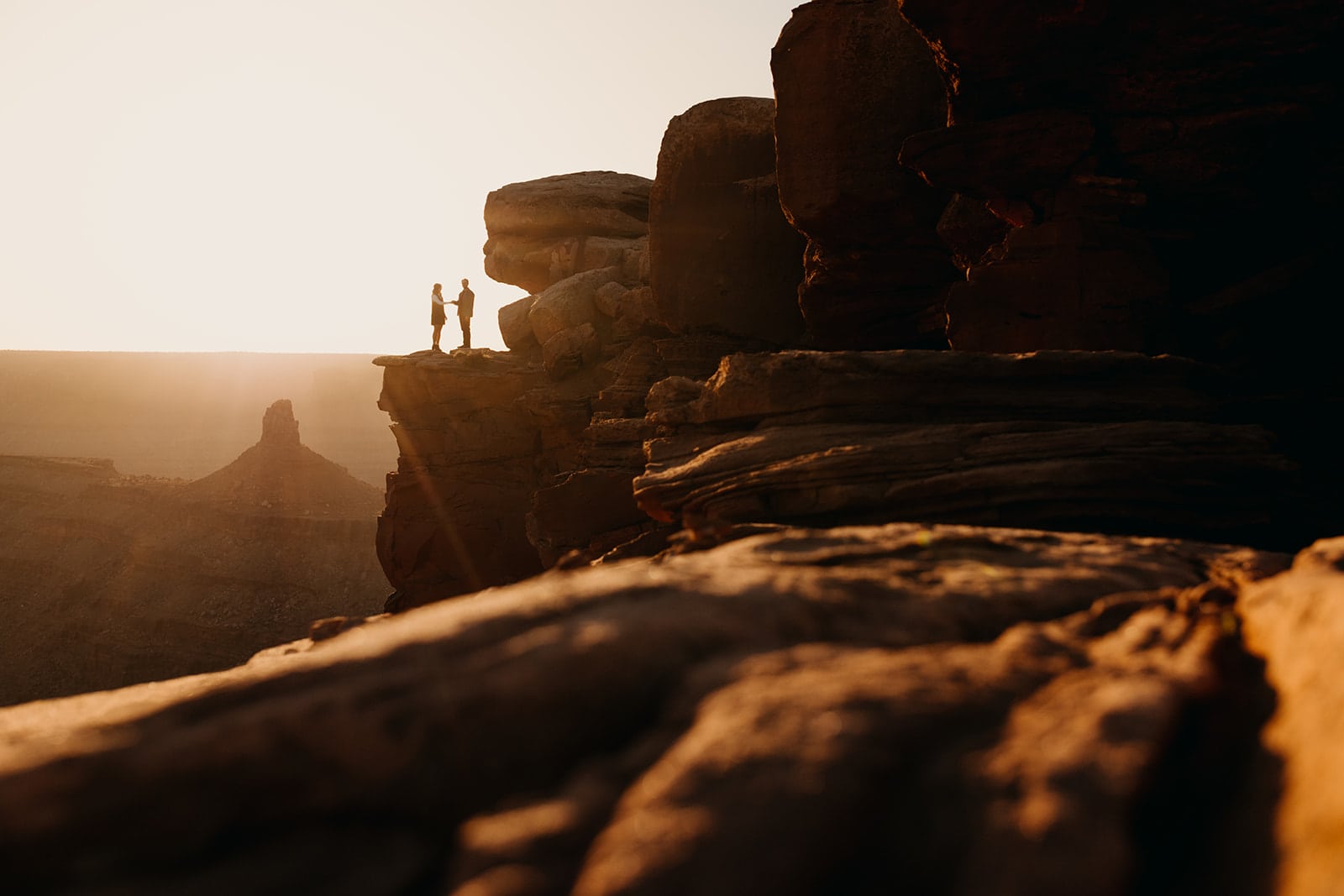 A man and woman stand together on a high up ledge at sunset in Moab