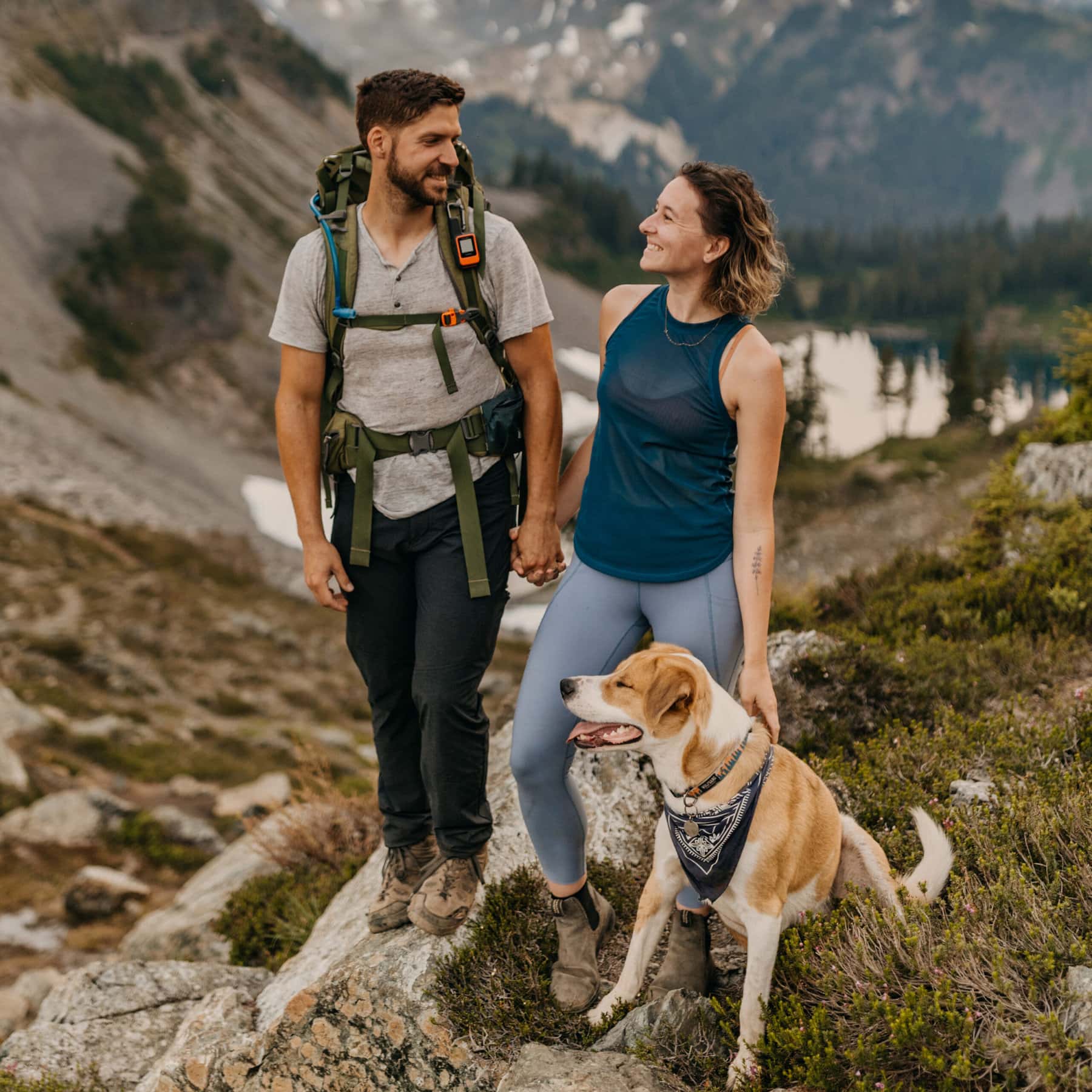 A couple stands for a portrait with their dog with Mt Baker in the background.