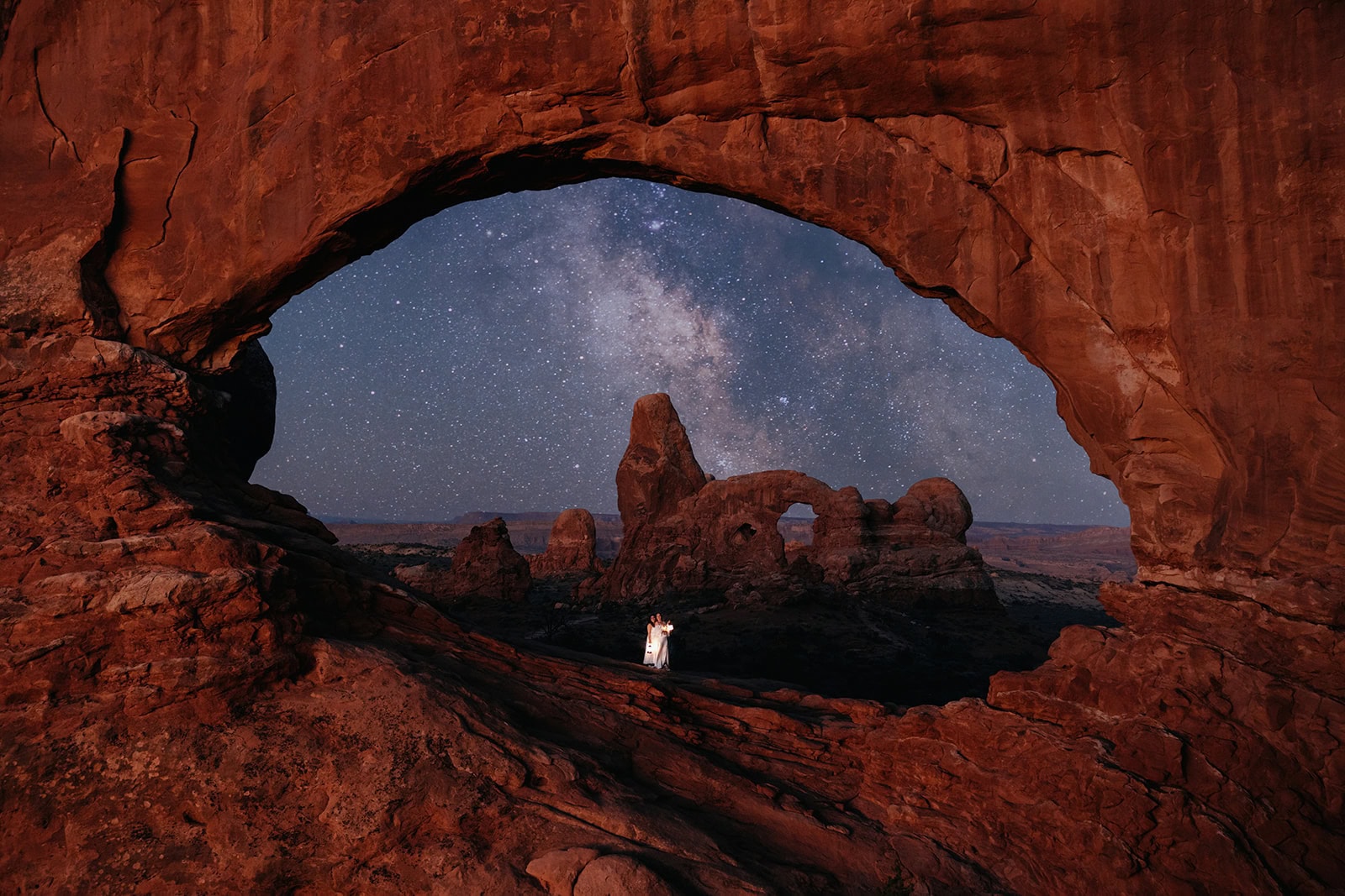A couple walks under an arch in Arches National Park.