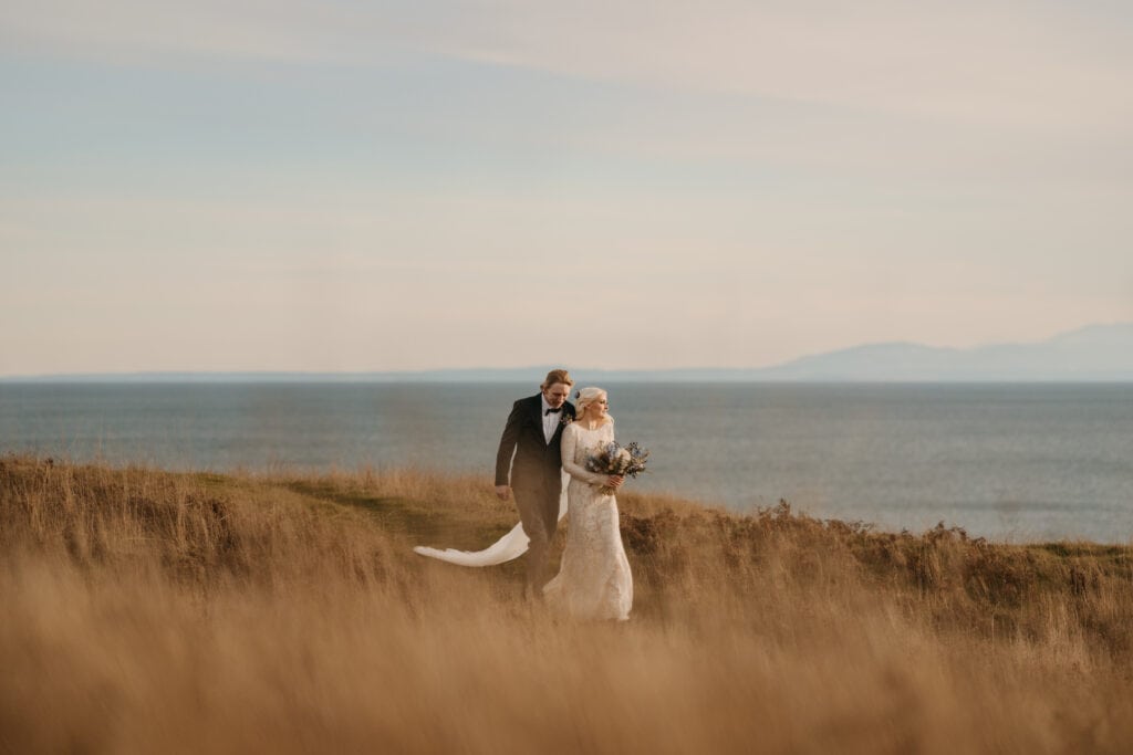 A couple walks together at sunset in their wedding attire looking out towards the mountains.