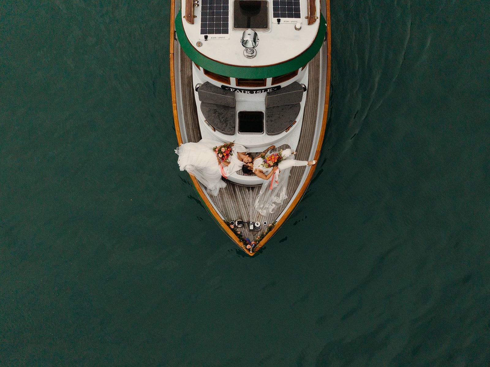 Two brides sit on the deck of a boat in the Fjordlands of Alaska.